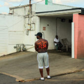 A black man with a tattoo on his back stand in a driveway