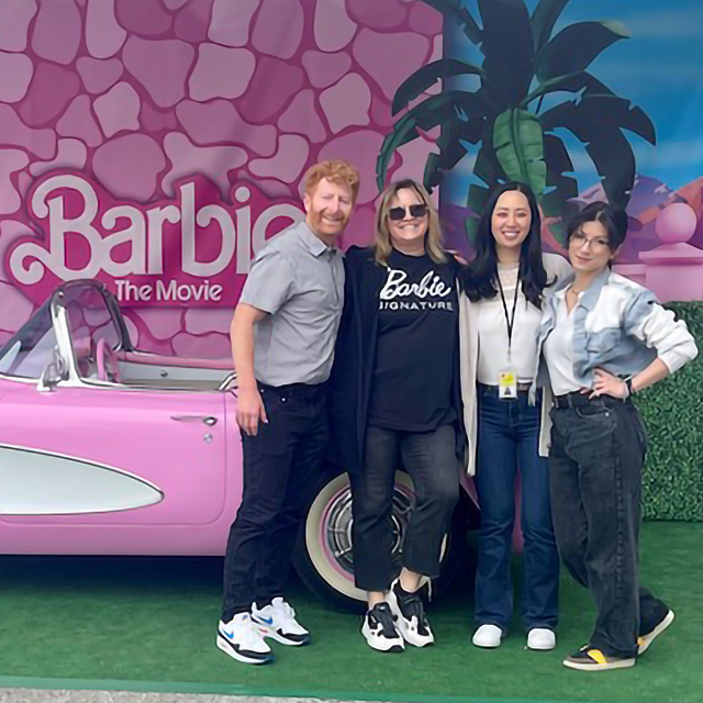 A group of designers stands next to a Barbie-themed car