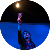 A woman holds a shadow puppet near a light bulb