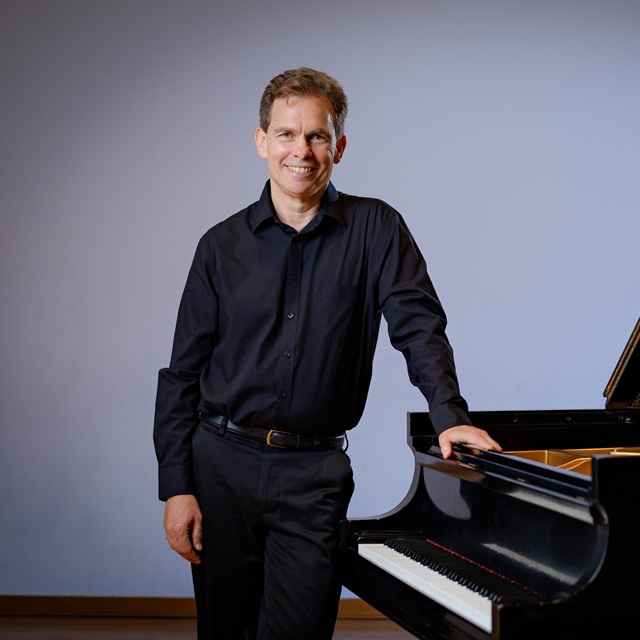 Peter Kairoff stands next to a piano