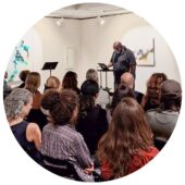 A Black man reads poems in an art gallery for a large audience