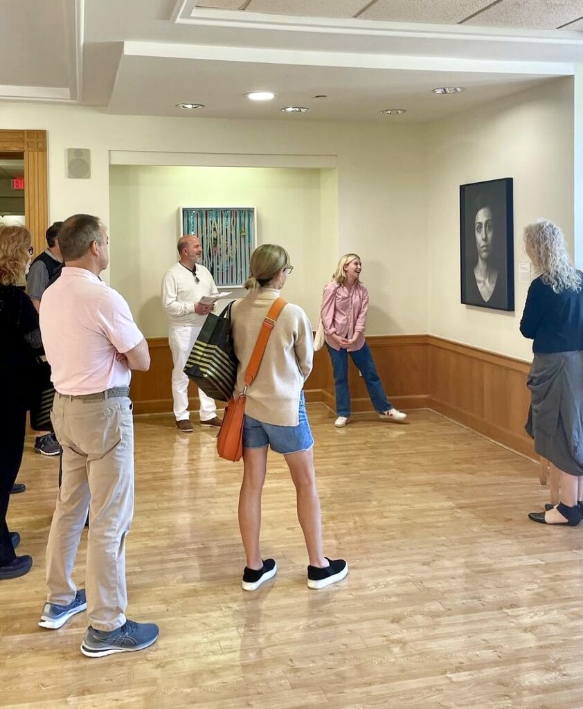 Image shows a student art tour guide and to visiting family members standing in front of a large, black and white portrait in Benson Student center of WFU. 