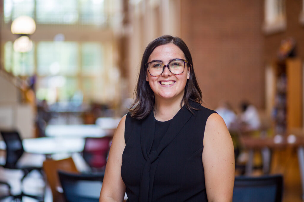 Davita DesRoches, a white woman with short brown hair and glasses, smiles in the atrium of ZSR Library at Wake Forest University.