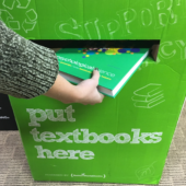 Text book donation drop box with a student dropping a textbook in the slot.