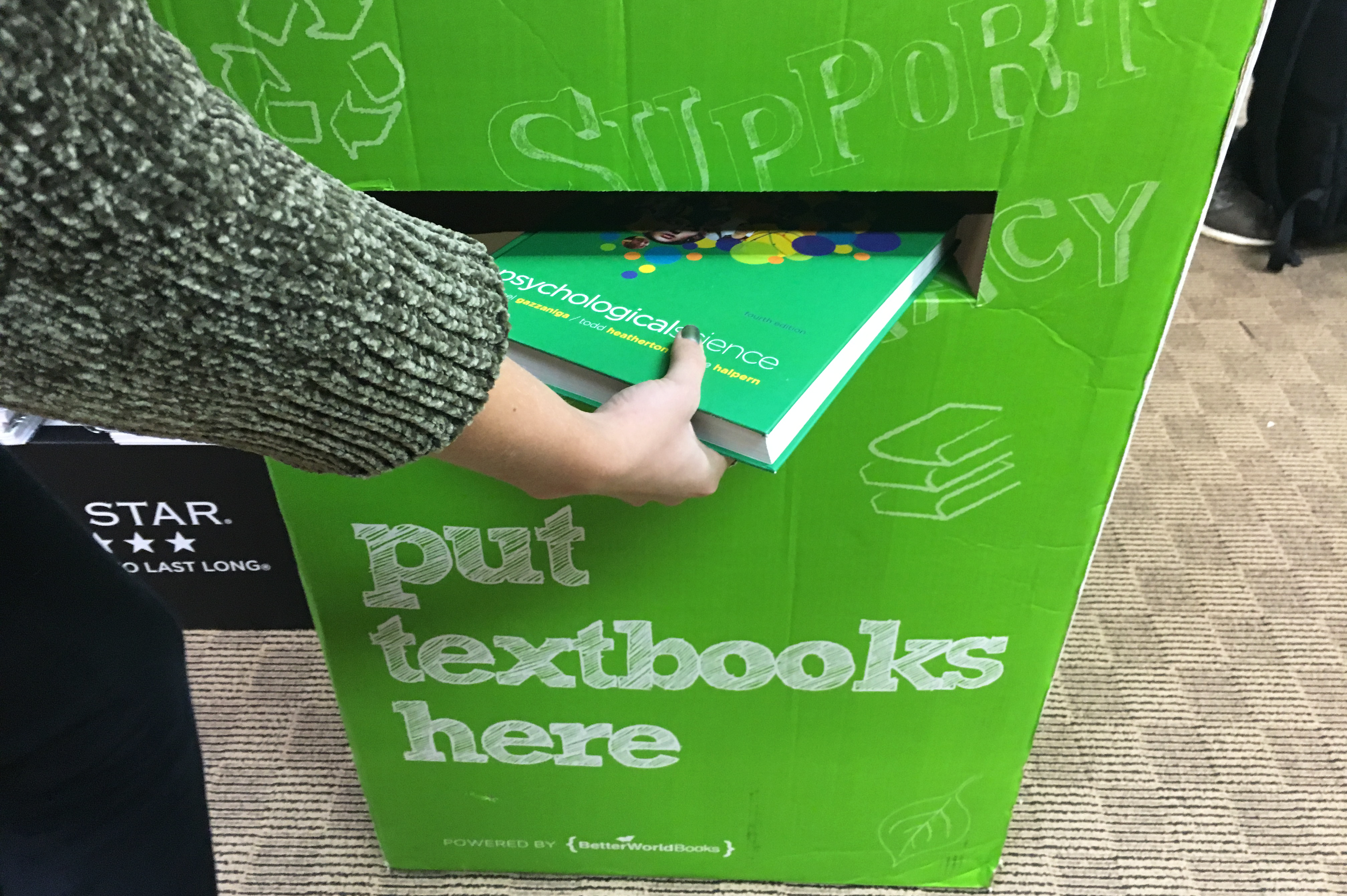 Text book donation drop box with a student dropping a textbook in the slot.