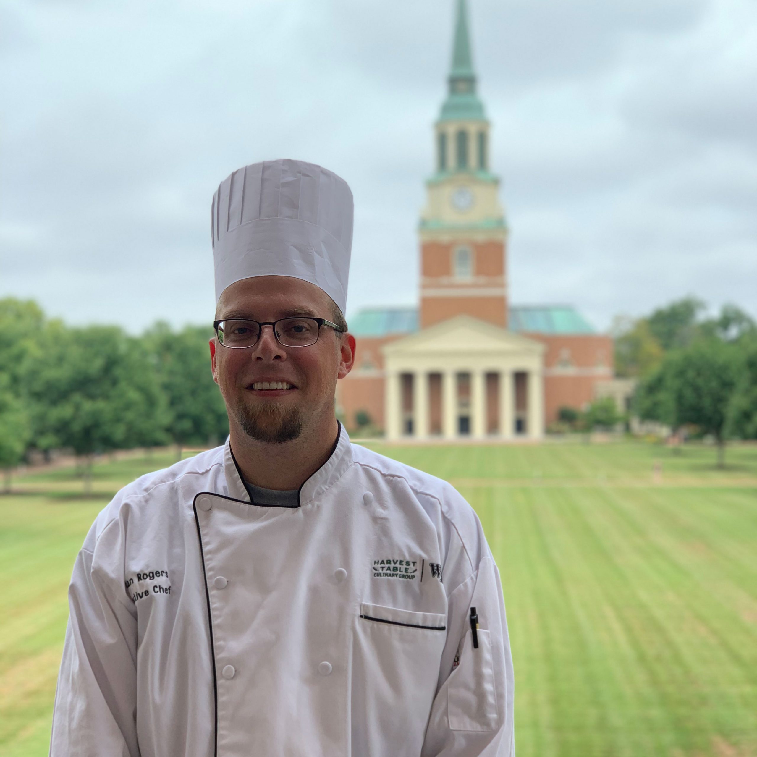 Chef Jordan standing on the Reynolda Hall Balcony with Wait Chapel viewed in the background.