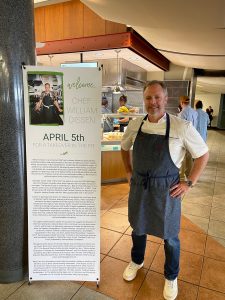 Chef William Dissen standing in the WFU Dining Hall next to a sign welcoming him to campus. 