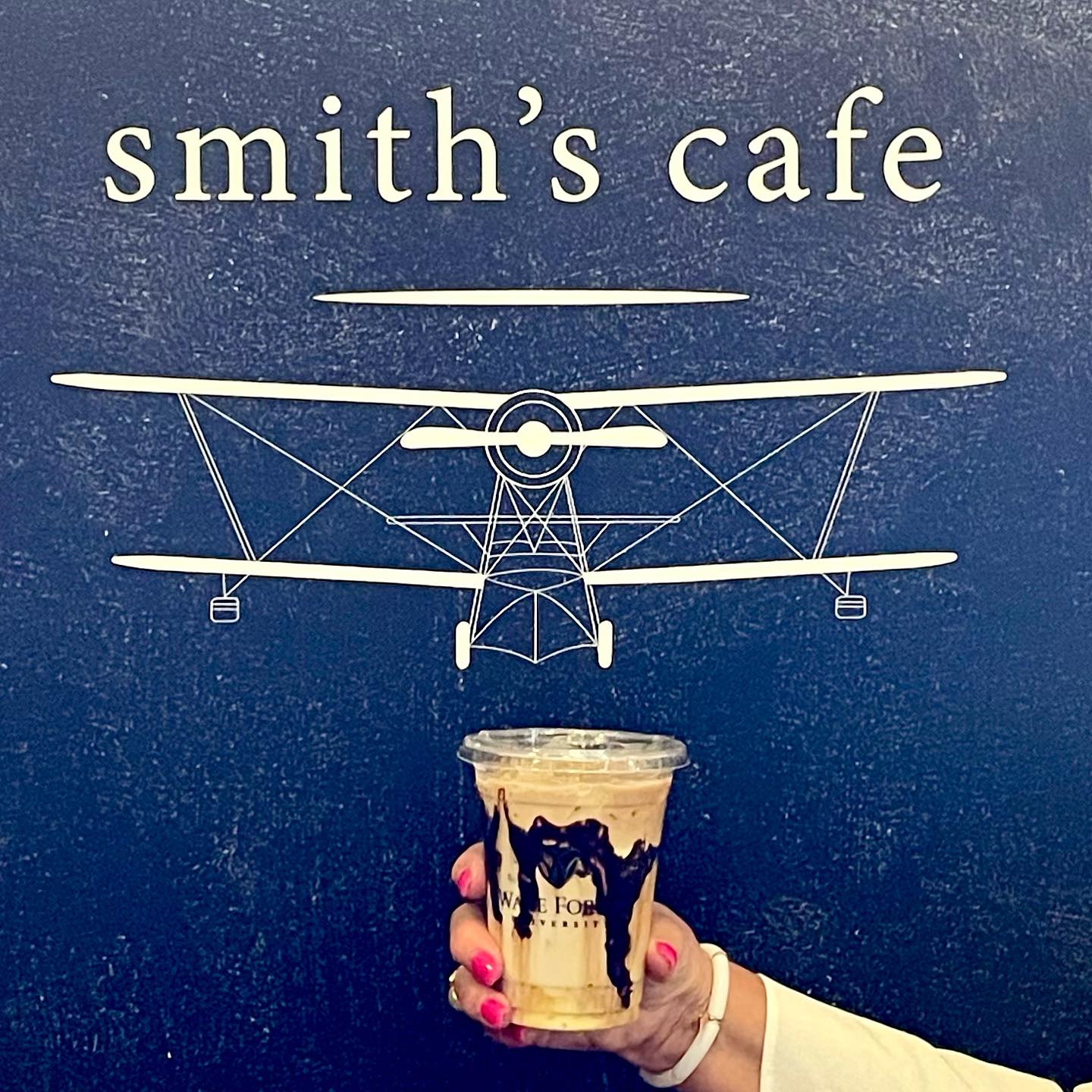 New coffee shop concept, Smith's Cafe. Located in ZSR library. Hand holding a coffee in front of the new Smith's Logo.