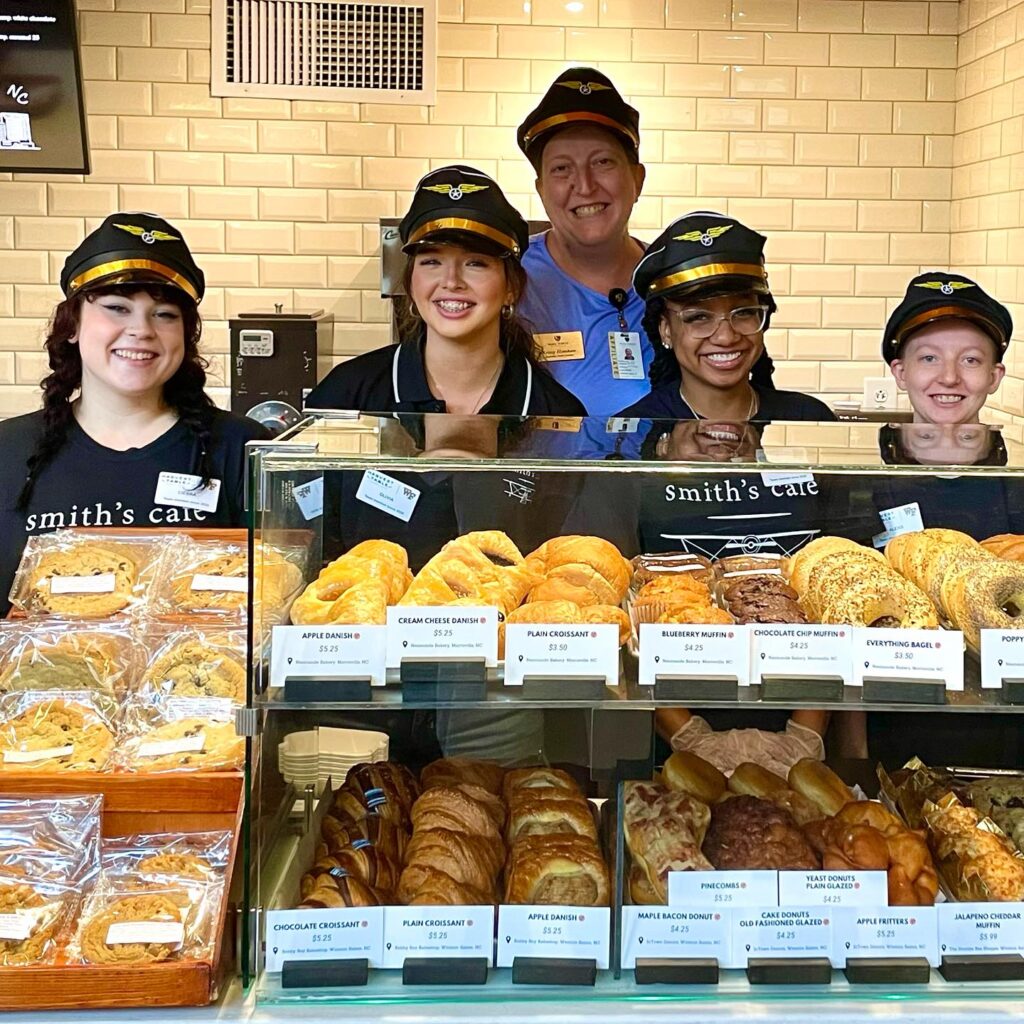 The Smith's Cafe team posing for a photo behind the counter of freshly baked local pastries. 