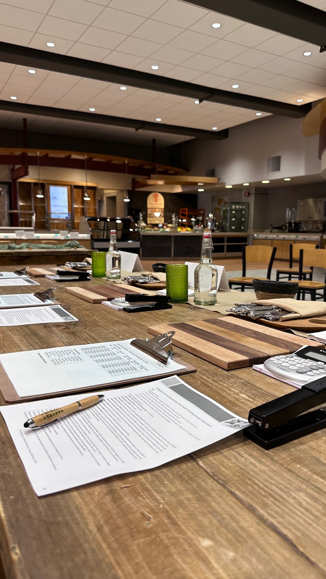 A neatly organized judging table setup with recipe descriptions on clipboards and score cards on a wooden table.