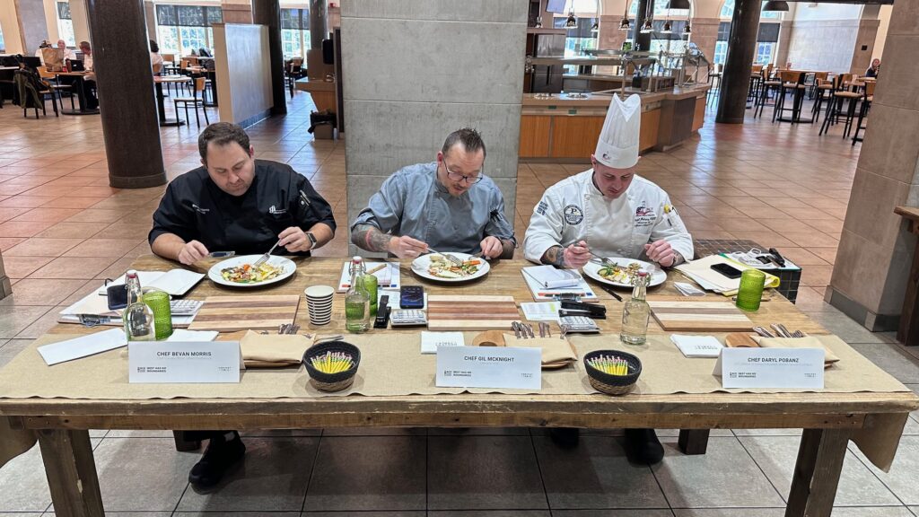 Panel of judges sitting at a table discussing scoring chef created dishes.