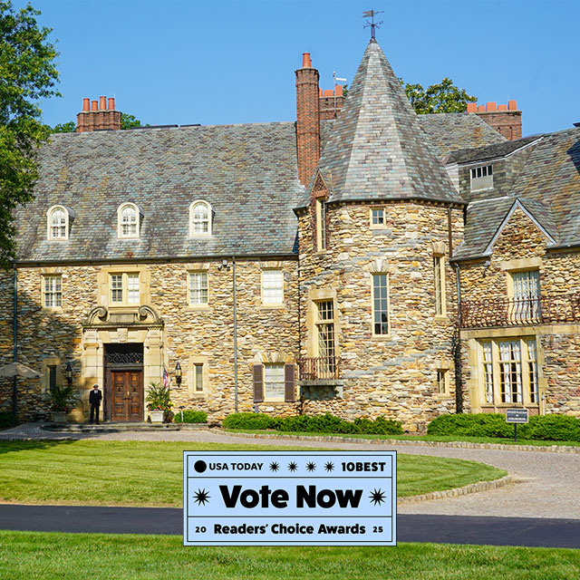 The Graylyn Estate, a historic stone mansion with slate roof and turret, nominated for USA TODAY’s 2025 10Best Readers' Choice Awards for Best Boutique Hotel. A “Vote Now” sign is displayed in the foreground.