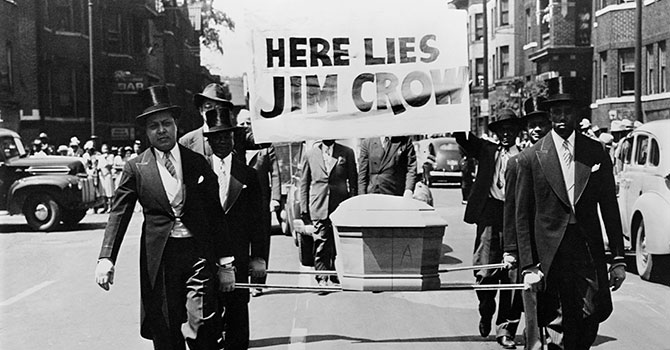 This photo depicts a symbolic funeral of Jim Crow. The African-American men are wearing tuxedos while carrying a coffin and a sign saying "Here Lies Jim Crow" as a demonstration against "Jim Crow" segregation laws in 1944.