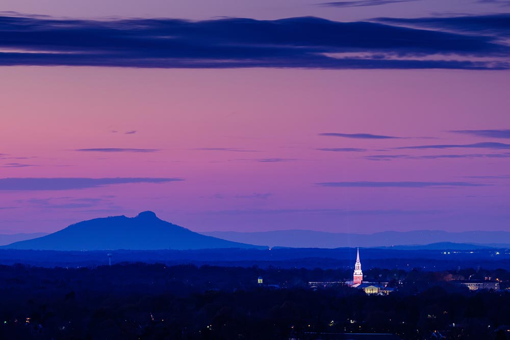 The bell tower of Wait Chapel rises over the Wake Forest campus at dusk as Pilot Mountain stands in the distance.