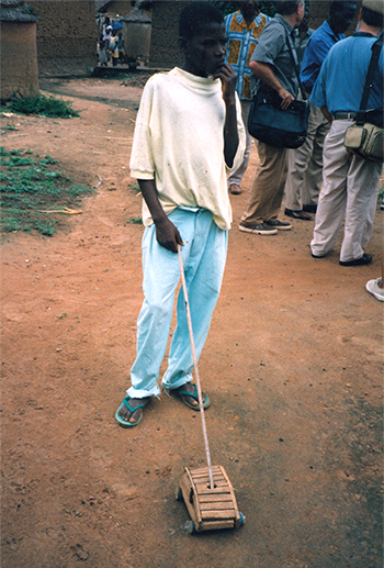 a boy playing with a toy car pushed by a stick