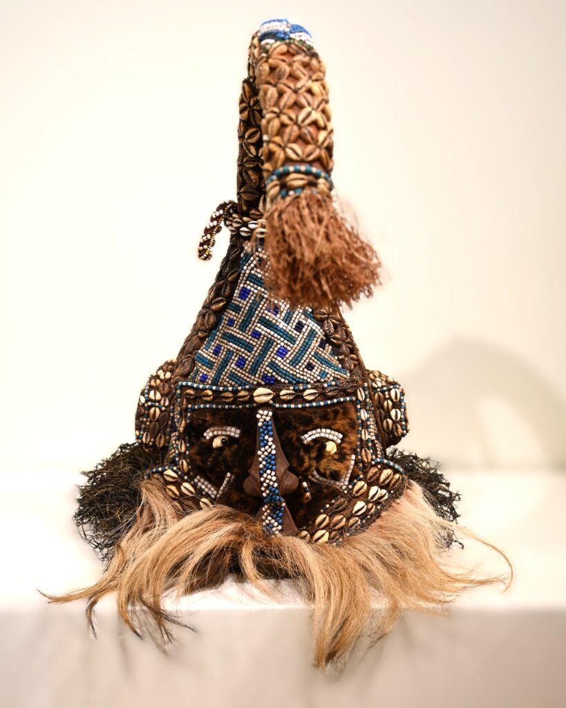 Mask with leopard fur on face, colorful glass beads, cowrie shells, and raffia.