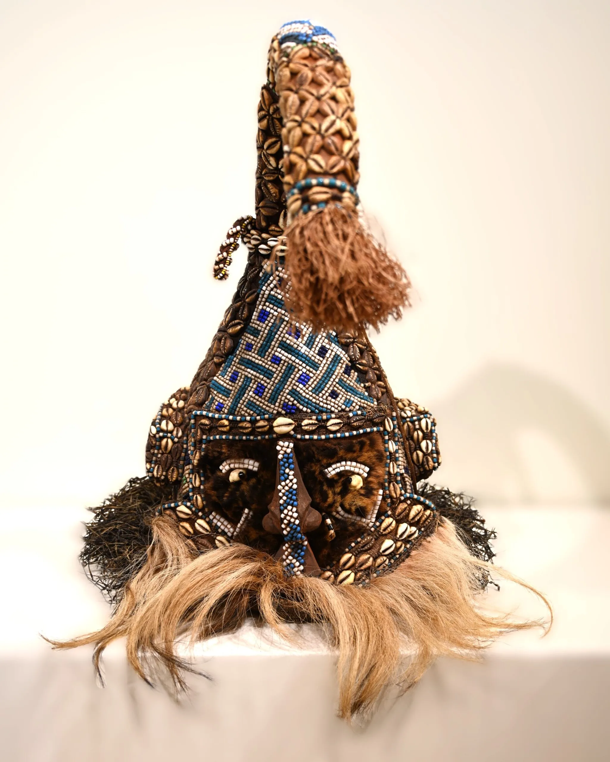 Mask with leopard fur on face, colorful glass beads, cowrie shells, and raffia.