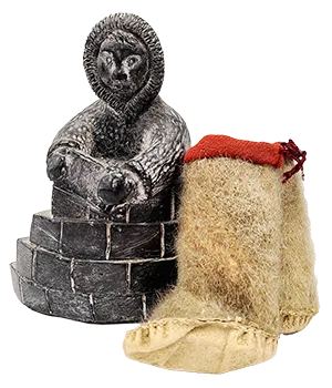 stone sculpture of figure building an igloo and miniature moccasins