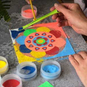 a woman's hands making a mandala made of colored sand