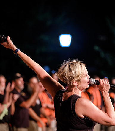 Allison Orr speaks into the microphone with her arm extended to rev up the crowd who have come out to the sho.