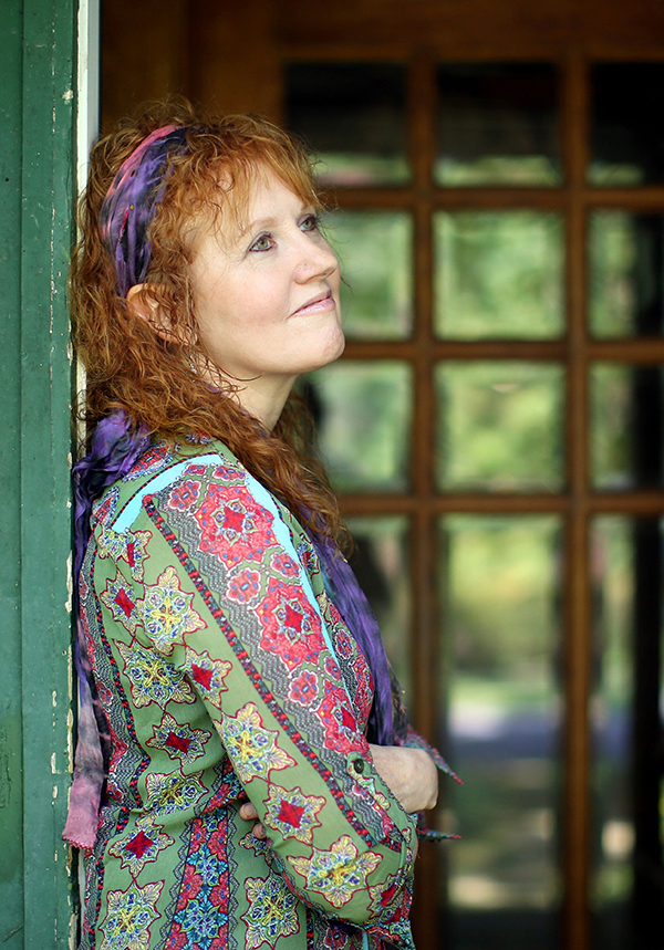 Jeanette Sorrell in a print dress and hairband gazes up as she leans against a doorway at her home.