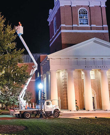 Scenes "From the Ground UP," a Telehandler bucket truck lifts an arborist to the top of a tree next to Wait Chapel