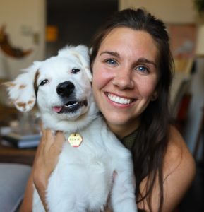 Johanna Beach ('15) smiles at the camera as she holds her white dog Howie in her arms while he smiles at the camera, too.