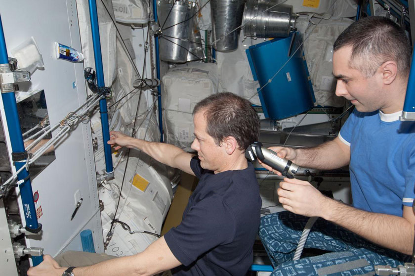 NASA astronaut Tom Marshburn (at left), Expedition 34 flight engineer, looks into a mirror as Russian cosmonaut Evgeny Tarelkin, flight engineer, gives him a hair trim in the Tranquility node aboard the International Space Station.