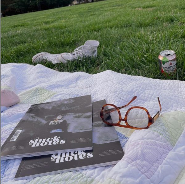 Two copies of second issue of Stuck in Notes magazine by founder and editor-in-chief Kelsey Willock ('15) and creative director Jordyn Albritton ('15), who were roommates at Wake Forest. The magazines are on a quilt on a grass with glasses, tossed aside sneakers and a drink can