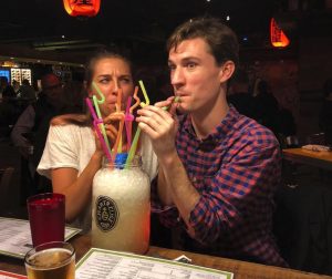 Alex Koblan ('13) and her husband, Bart Johnston ('12) sip on a large cocktail in a humorous photo at a bar.