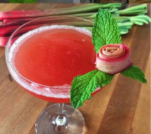 A pink cocktail with a rose and green leaves on the rim of a cocktail by mixologist Devin Kidner ('08)