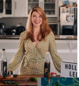 Devin Kidner ('08) stands smiling in front of her countertop at home in front of mixes and ingredients to make cocktails.