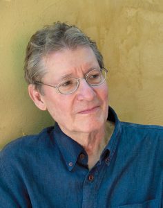 John Rosenthal headshot. John wears a denim shirt and glasses and looks into distance.