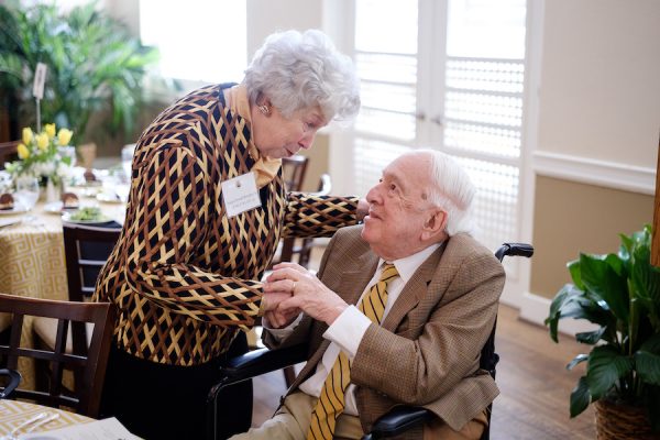 Susan Powell Brinkley holds the hands of Dr. Ed Wilson, seated, as she speaks with him.