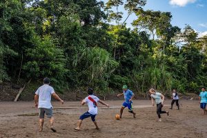 People play a game of soccer in a field with trees behind