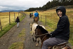 A student wearing a rain jacket and riding a horse turns around to smile at the camera