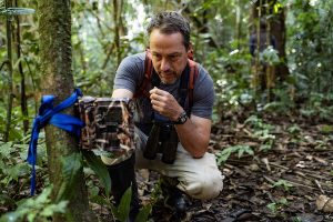 Miles Silman kneeling in the jungle working with binoculars around his neck