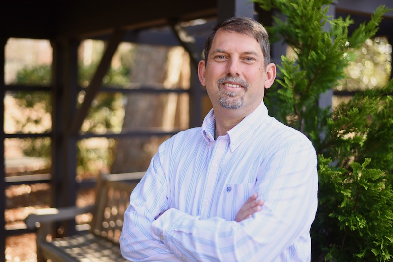 Jon Roethling smiles with his arms crossed for a headshot in Reynolda Gardens