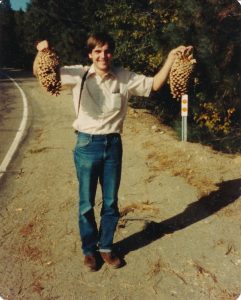 A young Frank Telewski smiles holding two large pinecones