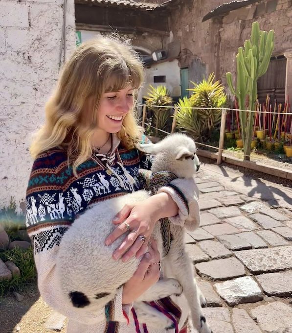 Una Wilson holds a baby animal in her arms and smiles down at it.