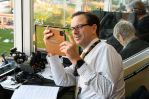 John Currie takes a photo with his iphone in the radio booth at Truist Field.