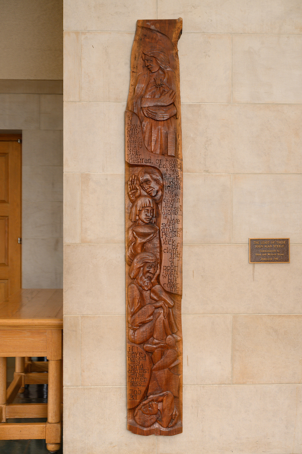 Long, vertical wooden sculpture with faces and text from Job carved in the sculpture.