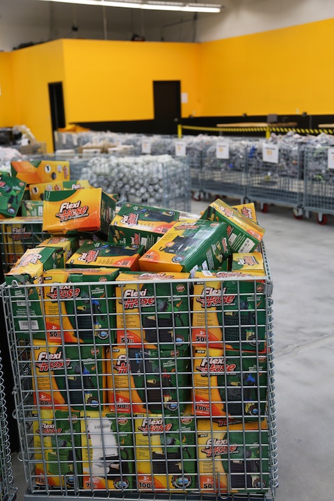 A bin filled with green garden hoses in yellow packaging at Jack Laughlin's BinStar store.