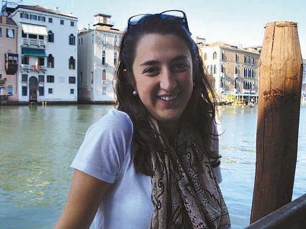 A student sitting by the Grand Canal. She wears a white shirt and a tan scarf and has glasses on top of her head.