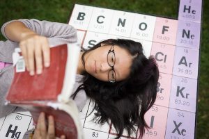 A student lies on the "Periodic Table Table" picnic table near Salem Hall while reading.