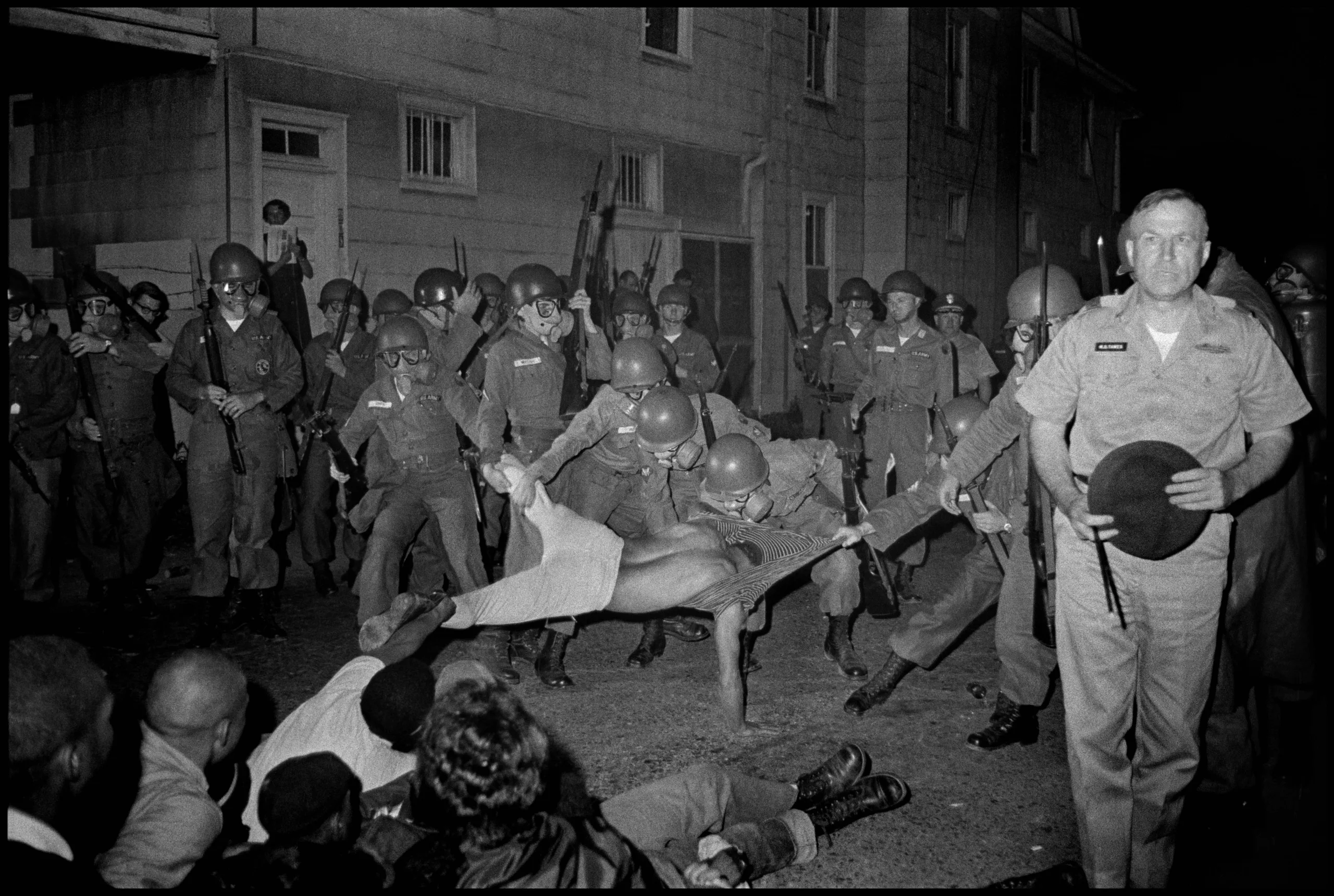 Black-and-white photo of National Guard soldiers pulling a demonstrator one way while seated demonstrators, with one person pulling him from the other side, resist.
