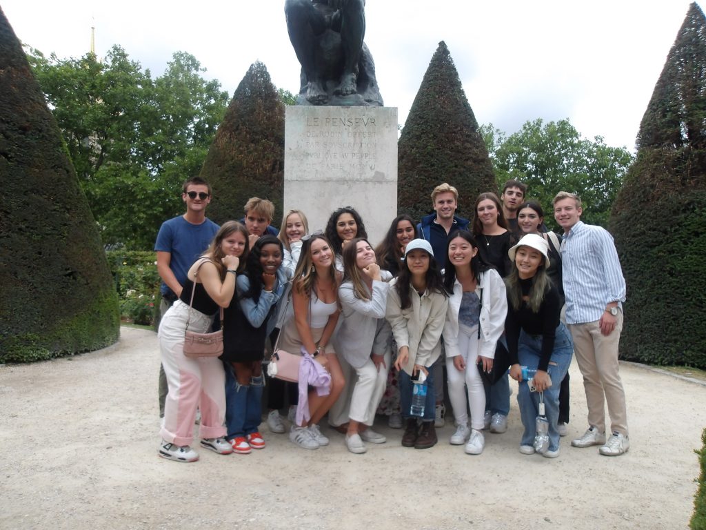 A large group of students posing in front of a sculpture in a garden in Tours