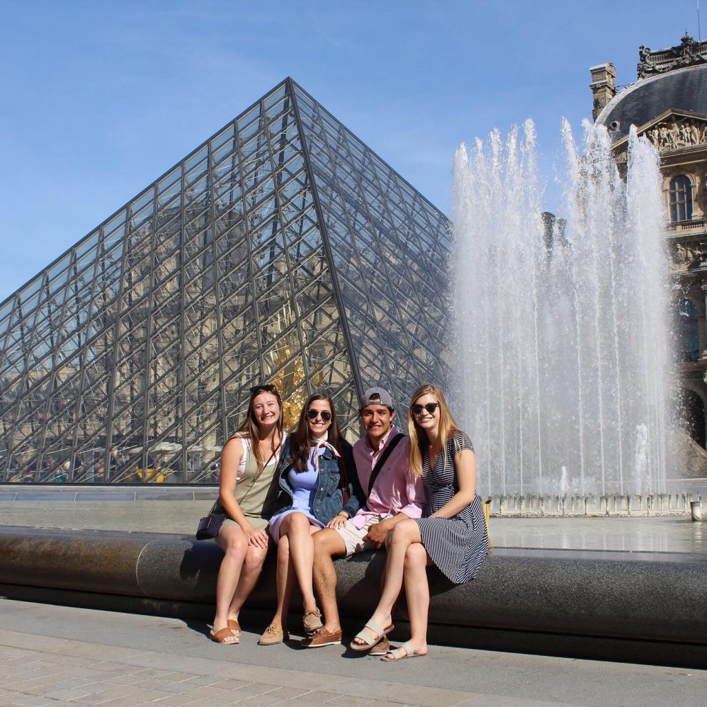 Four students sitting in front of the Pyramid at the Louvre