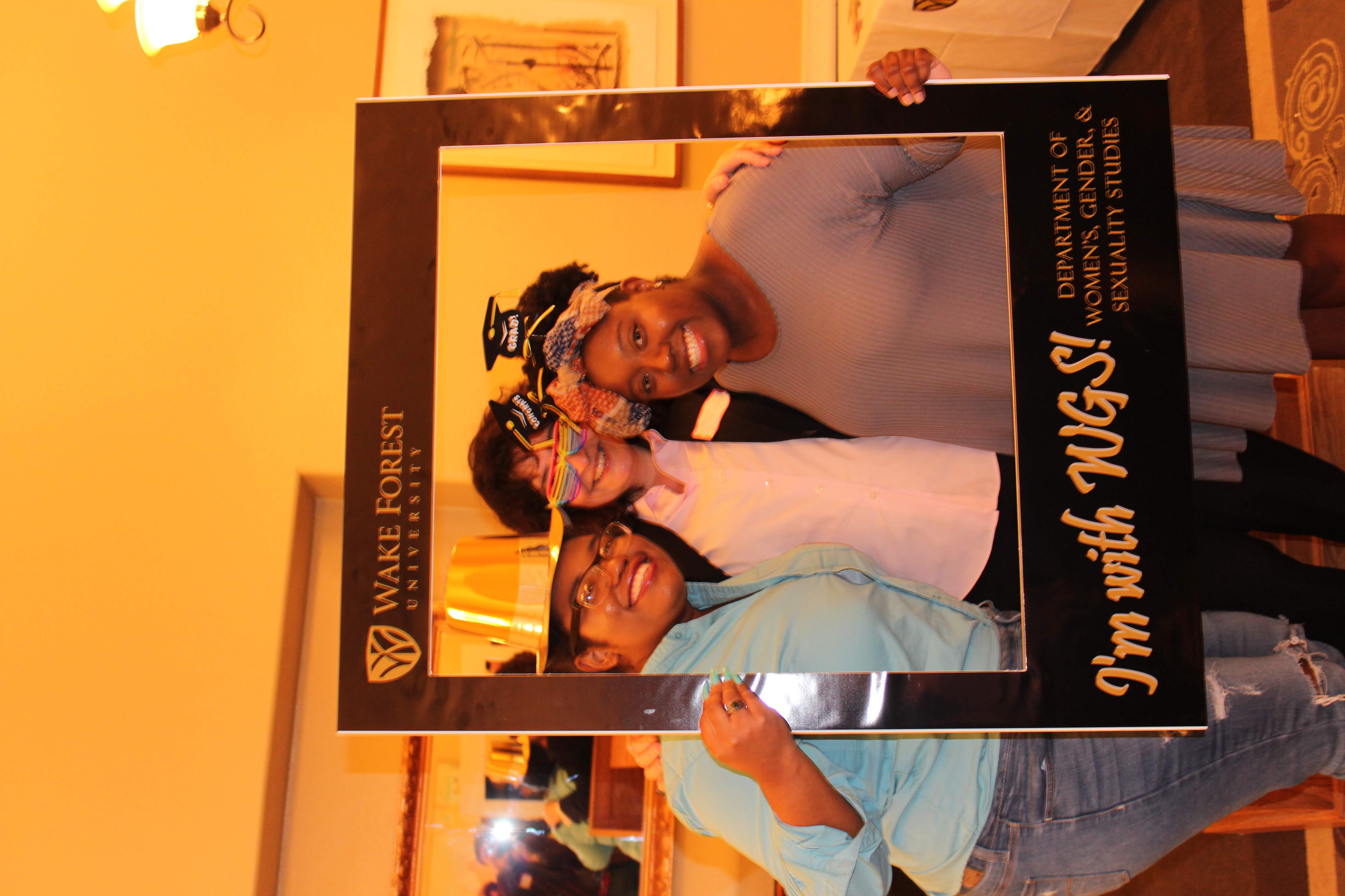 Three WGSS students smiling while wearing photo props