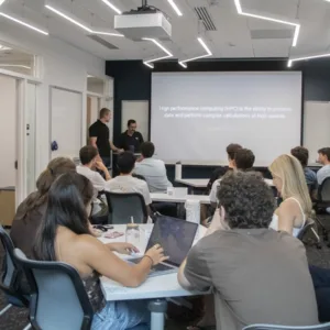 Wide classroom view of FYS 100 students seated at tables while two presenters introduce high-performance computing on a projected slide.